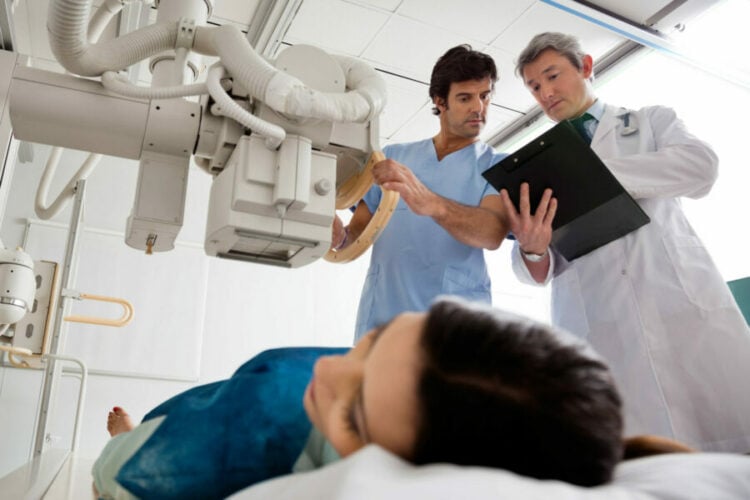 Physicians consulting a chart while a patient has an x-ray taken