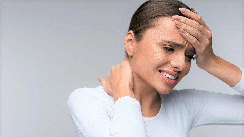 Woman grimacing from pain while holding her forehead and neck