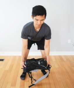 man bending forward in a dead-lift position preparing to lift a heavy backpack