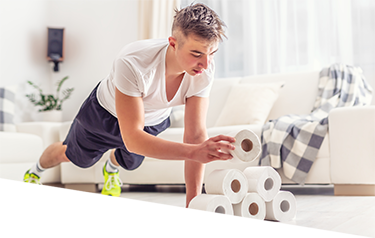 Young man in a plank exercise position stacking rolls of toilet paper into a pyramid