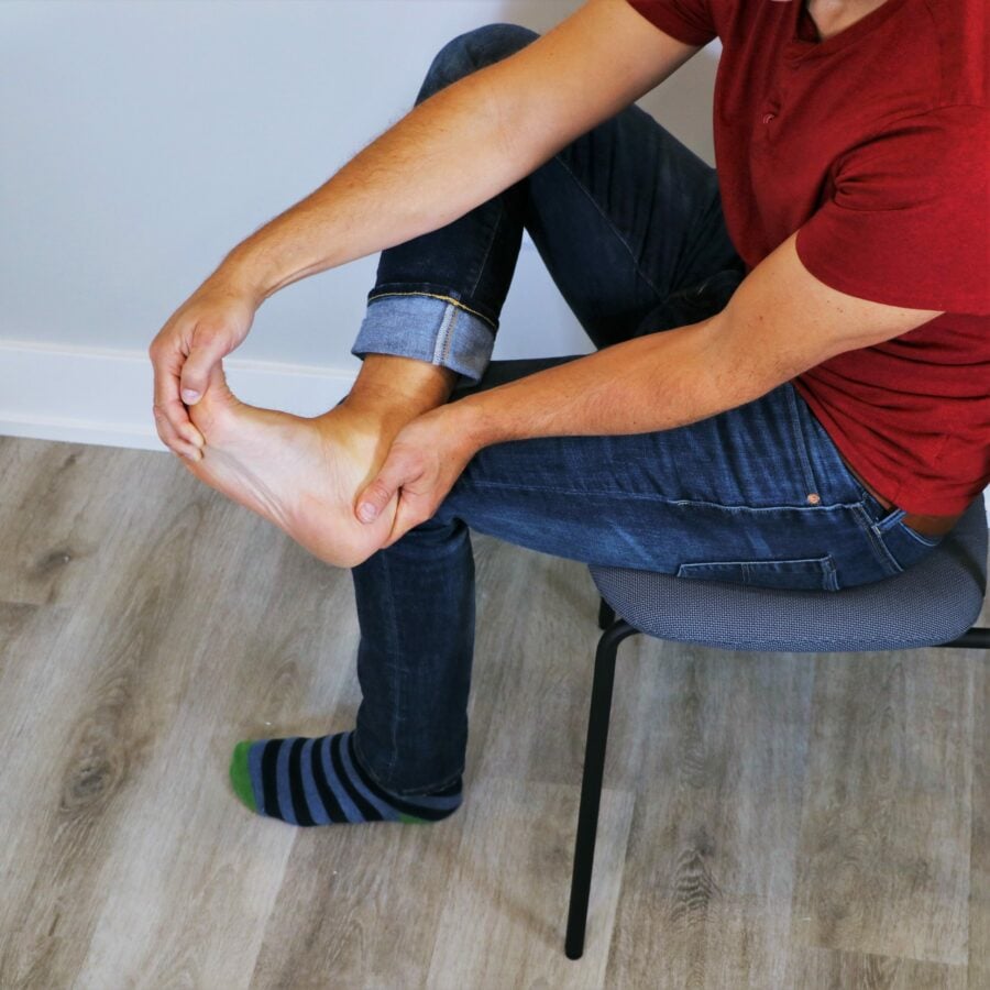 man holding foot while performing a sitting plantar fasciitis stretch in a chair